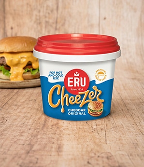 Pot Cheezer Original Cheddar met een hamburger met kaassaus in de achtergrond op een houten tafel.